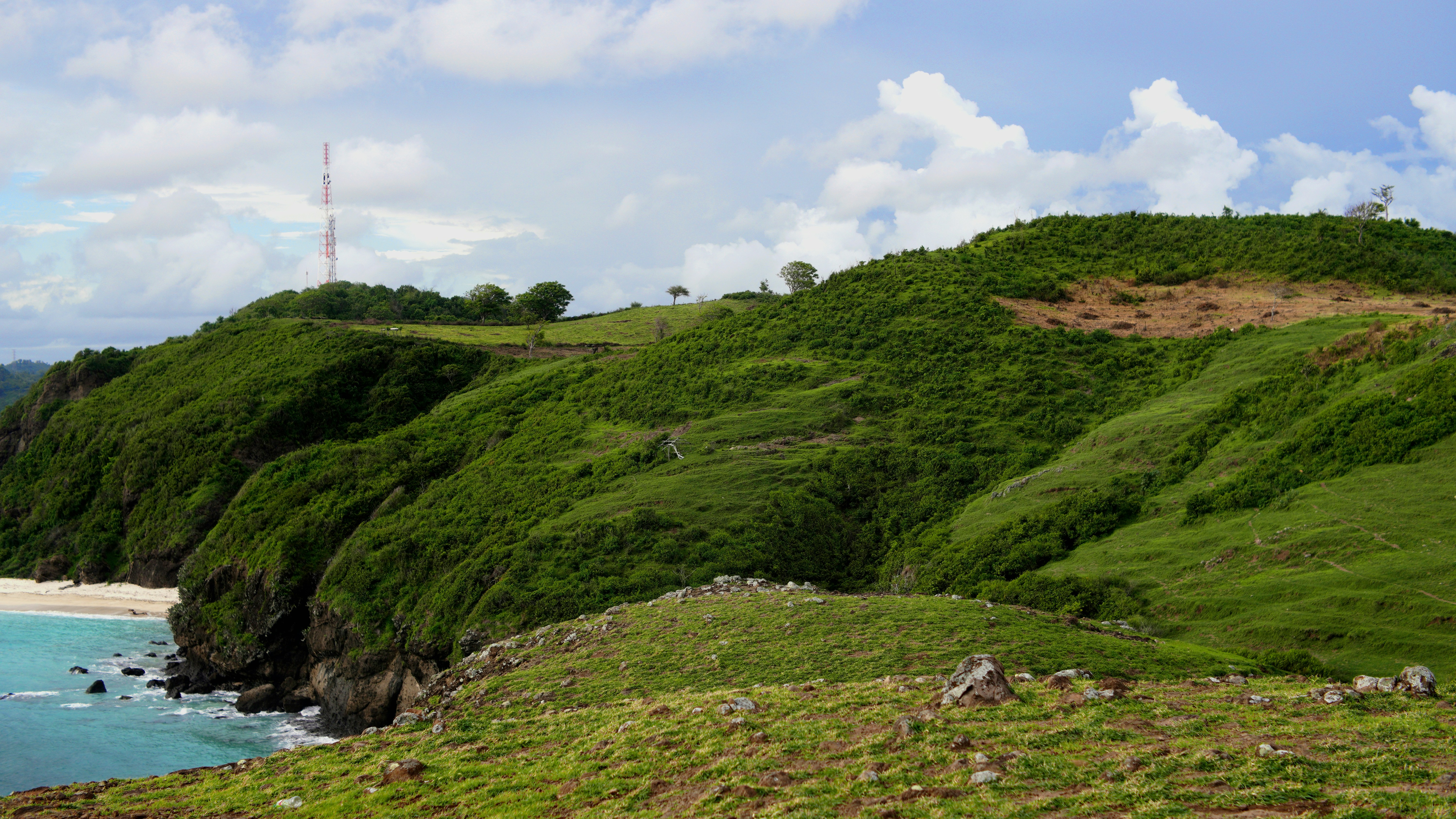 A grassy hill with a body of water in the background - Lombok