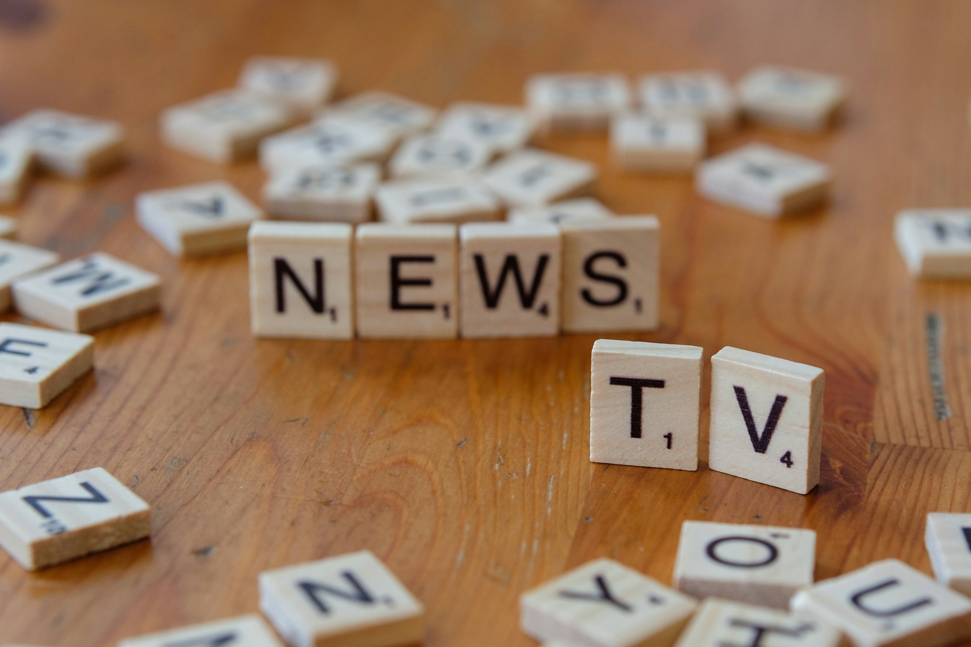 A wooden table topped with scrabble tiles spelling news