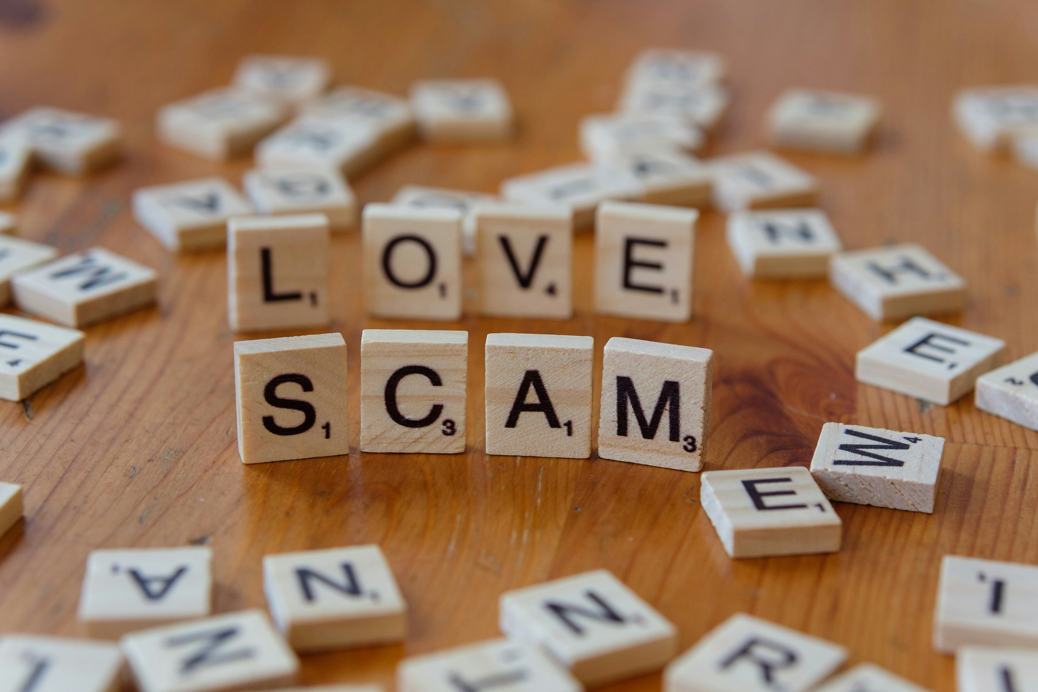 Scrabble letters spelling love scam on a wooden table