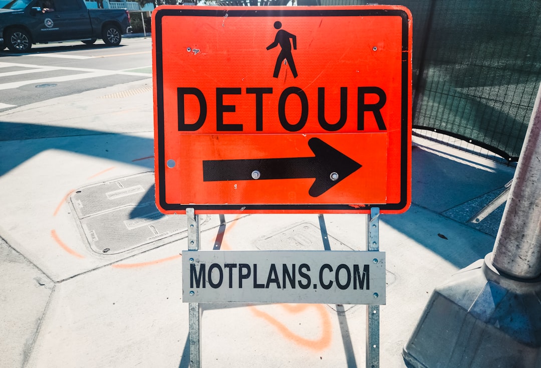A detour sign on the side of the road, An orange detour sign is a temporary traffic control device used to redirect vehicles from their usual route due to roadwork, construction, or other obstructions. The bright orange color makes it highly visible to drivers, signaling that a detour is in place. These signs are crucial for managing traffic flow and ensuring safety in construction zones or areas where roads are closed. Historically, detour signs have been used in road safety efforts to prevent congestion and accidents, guiding drivers along alternative routes until work is completed.