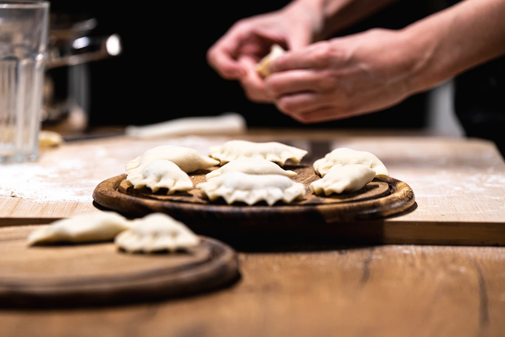 Hand shaping dumpling wrappers during food preparation; application photograph