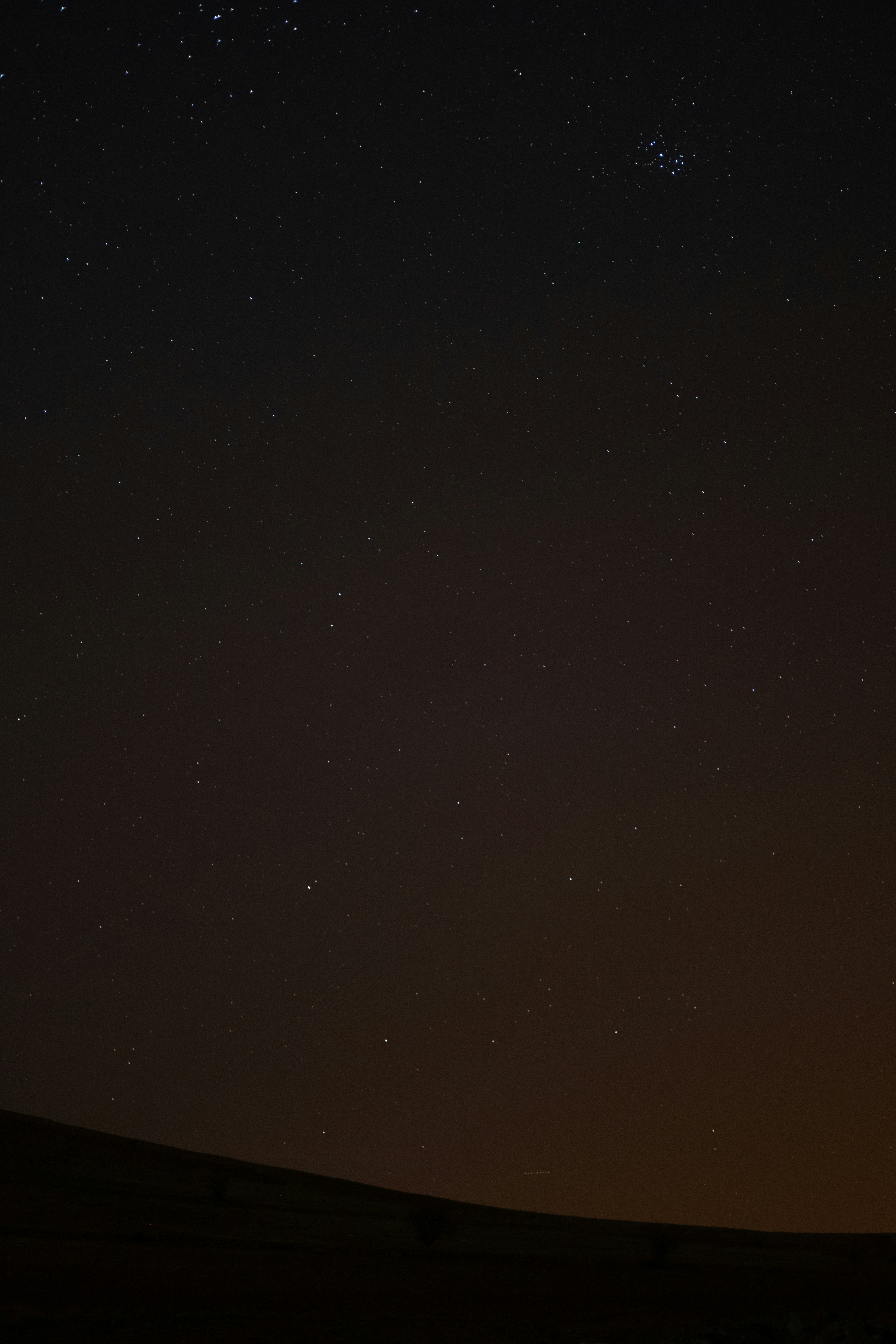 The night sky is filled with stars above a hill