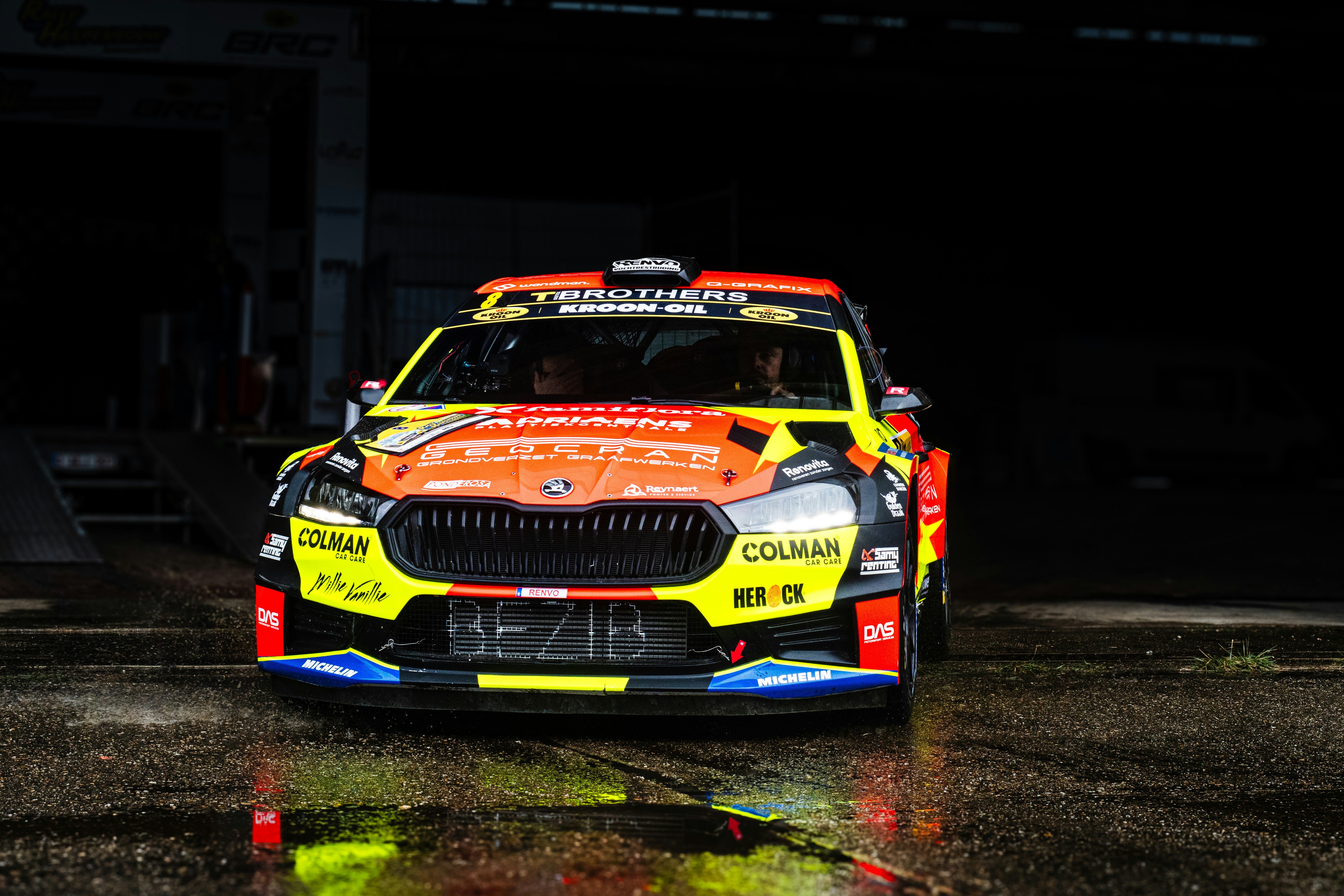 A yellow and red car driving on a wet road