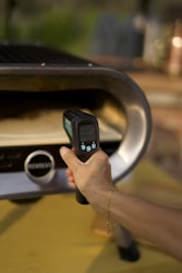 A person holding a cell phone in front of a grill