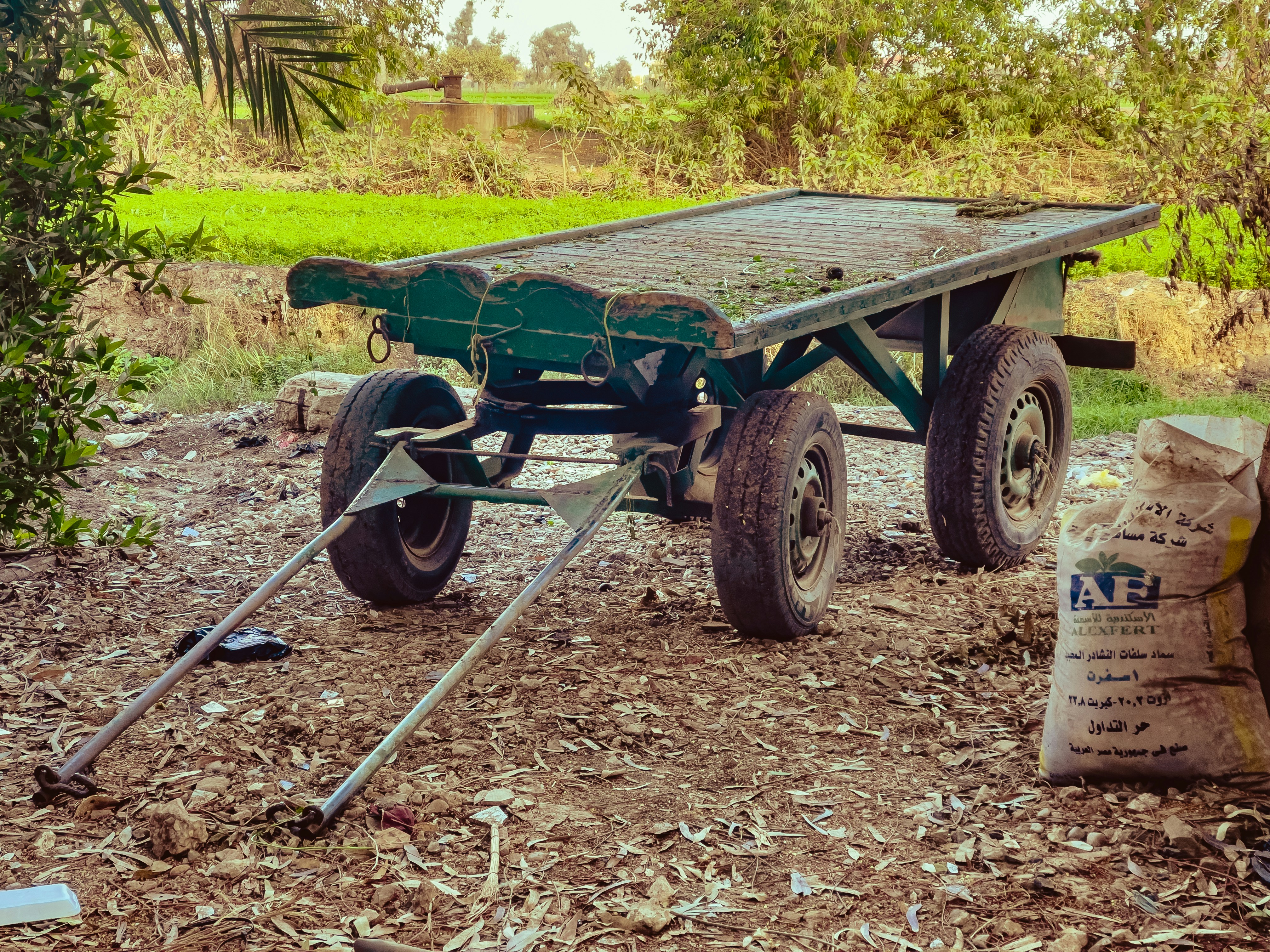A green wagon sitting on top of a dirt field