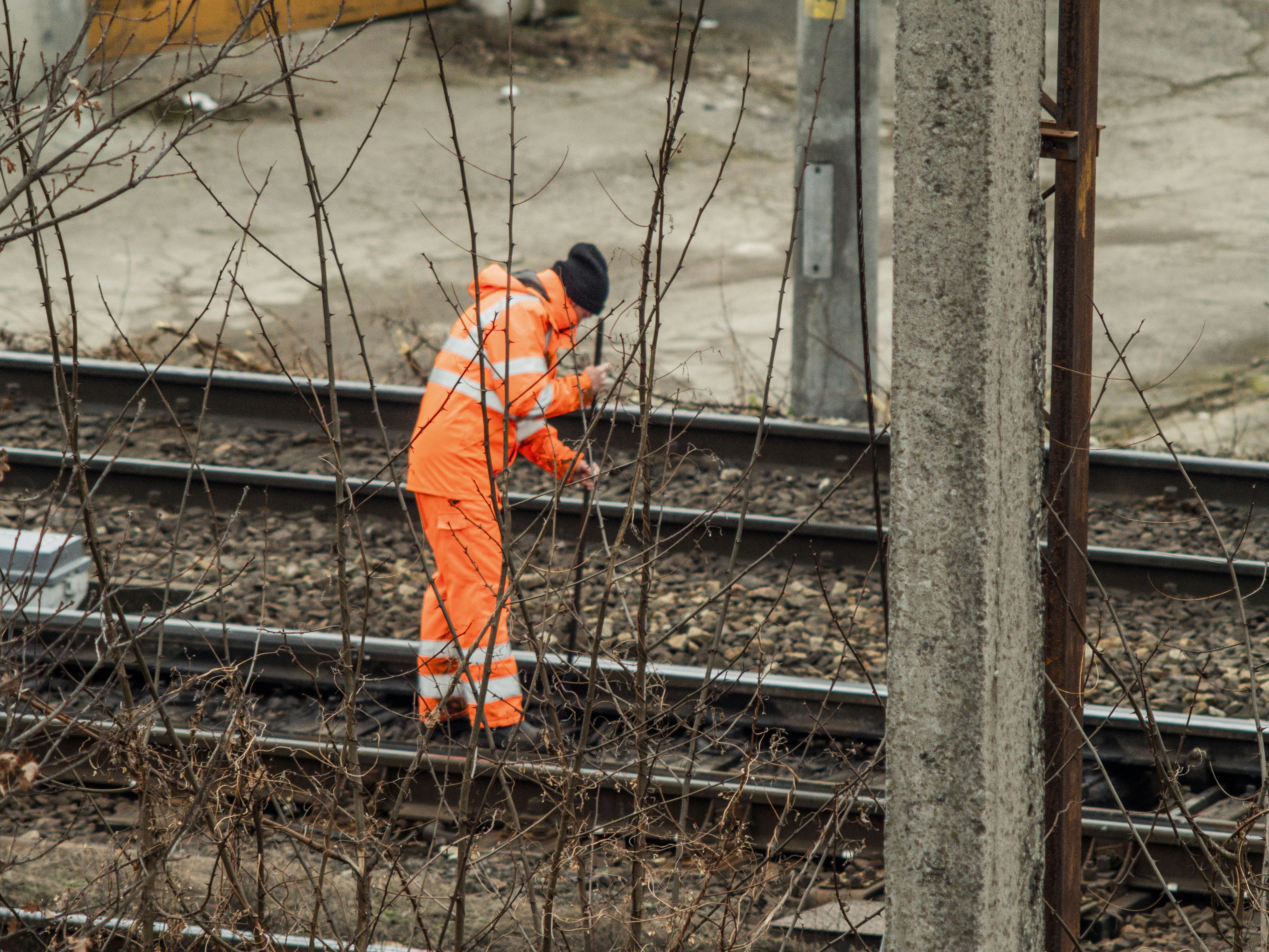 A railway worker inspecting a section of the newly installed concrete fence along the tracks, with safety gear on and a tool in hand, ensuring its integrity.