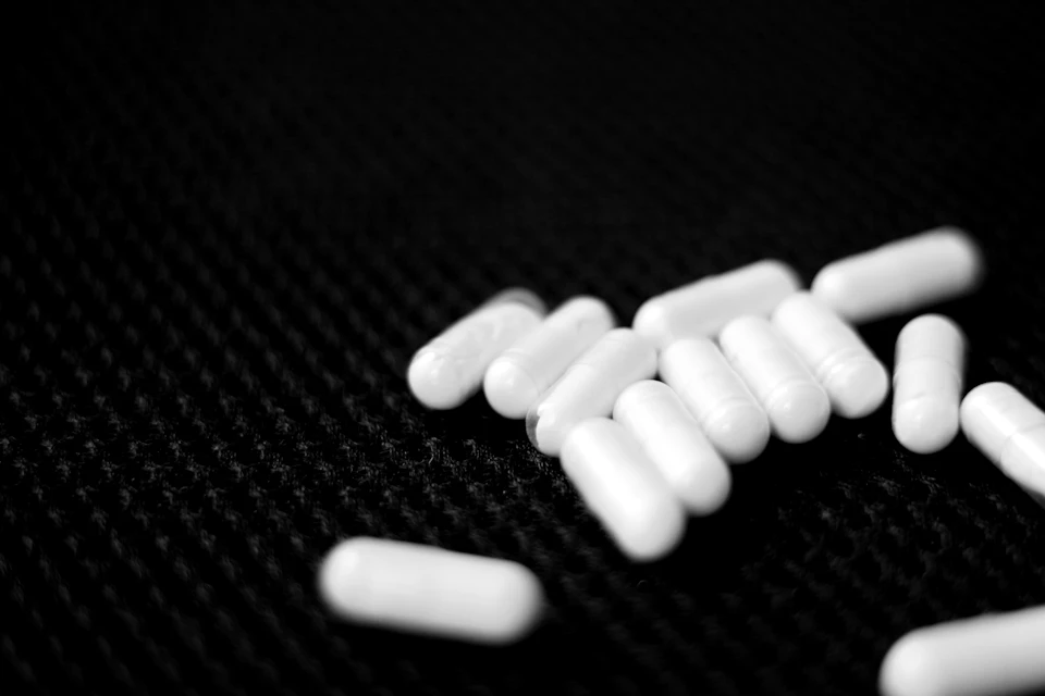 Close-up view of white pills scattered on a black background in random orientation