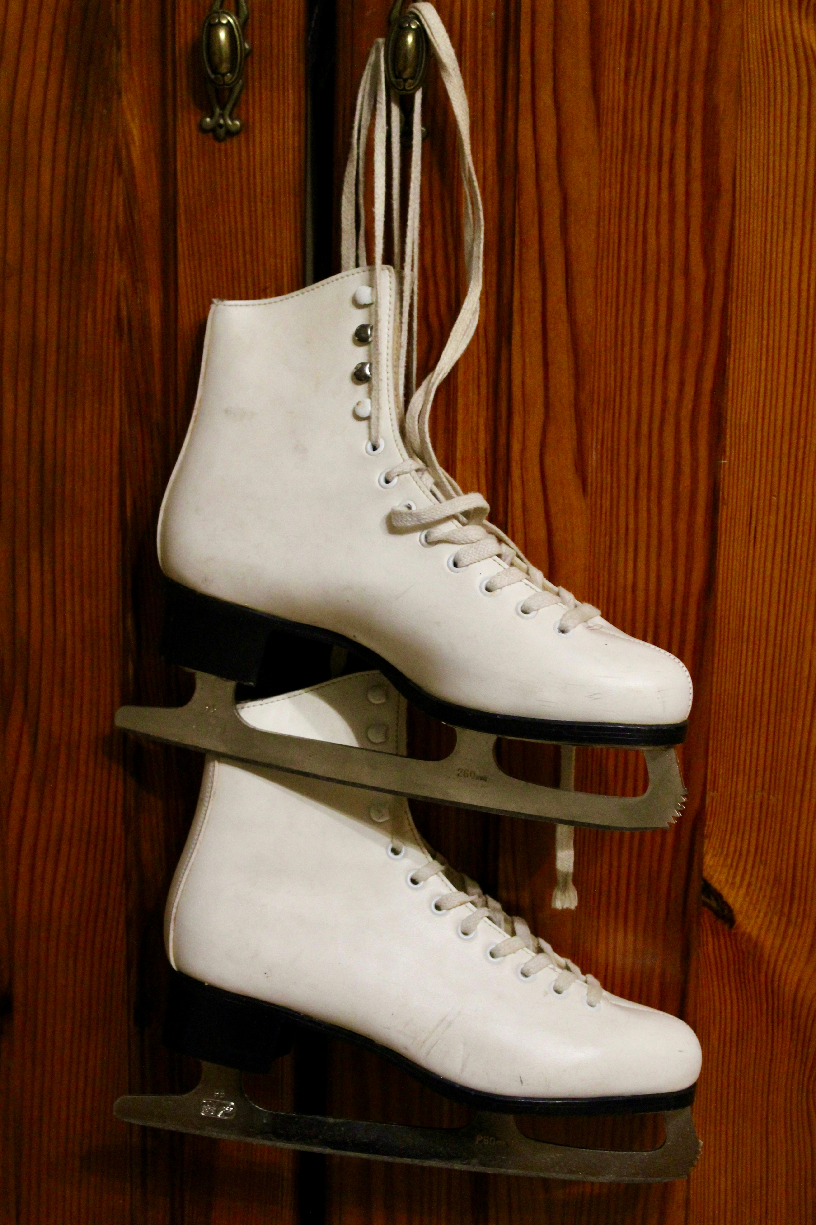 A pair of white ice skates hanging on a wooden wall