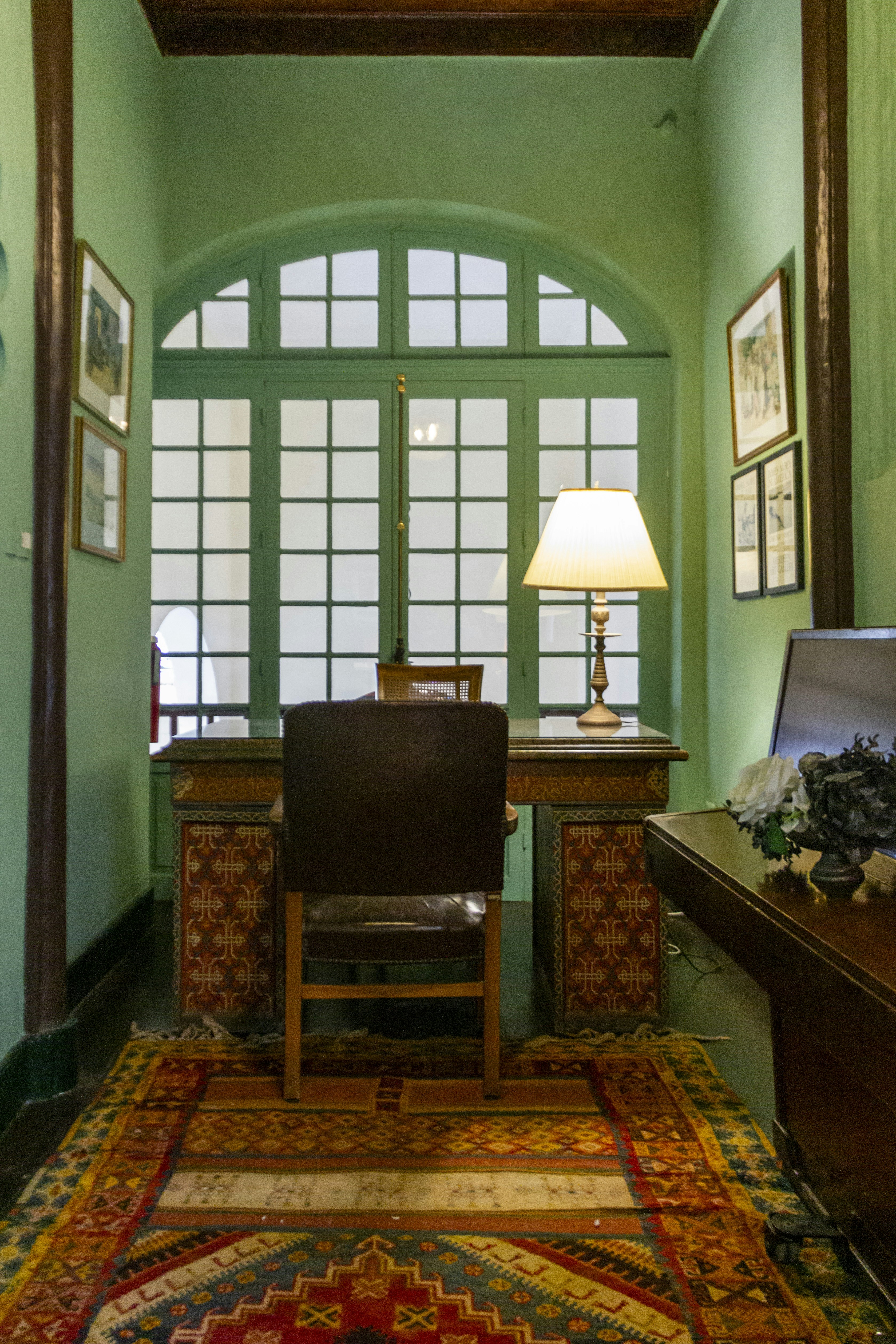 Una habitación con un escritorio, una silla, una lámpara y cuadros en la pared