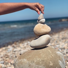 A person stacking rocks on a beach with the ocean in the background