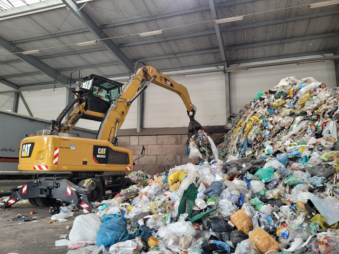 A wheeled loader working a deep pile of mixed municipal waste inside a storage hall.