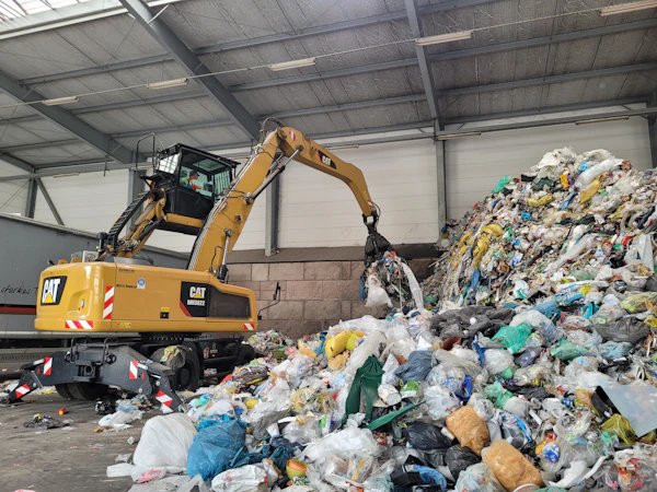 A wheeled loader working a deep pile of mixed municipal waste inside a storage hall.