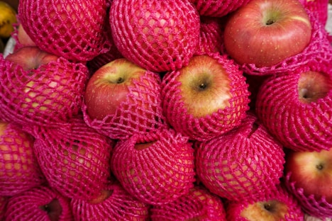 A pile of red mesh bags filled with apples
