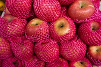 A pile of red mesh bags filled with apples