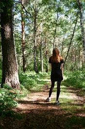 A woman in a black dress walking through a forest