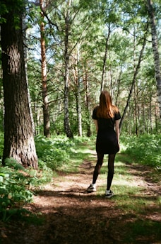 A woman in a black dress walking through a forest