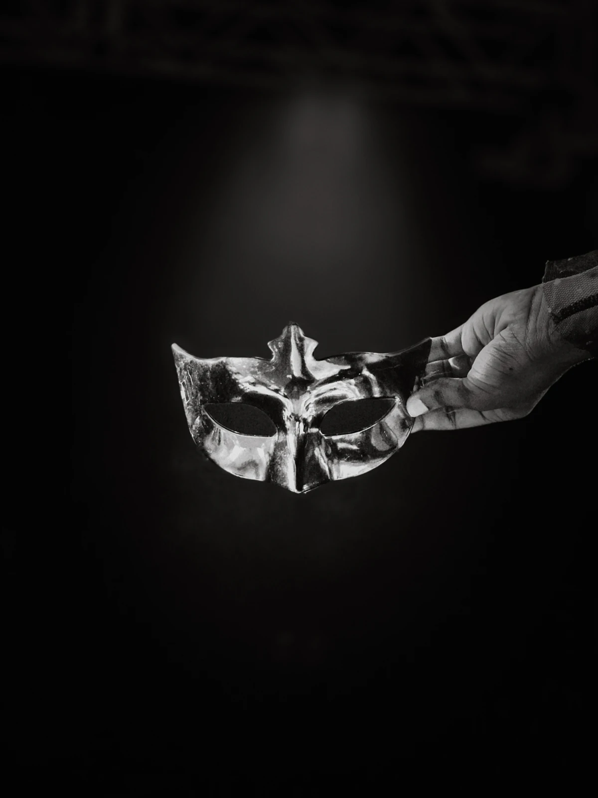 Hands holding a masquerade mask in shadow