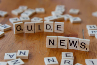 A wooden table topped with scrabble tiles spelling the word guide news