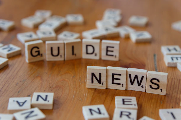 A wooden table topped with scrabble tiles spelling the word guide news