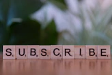 A wooden block spelling subscribe on a table