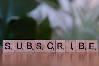 A wooden block spelling subscribe on a table.