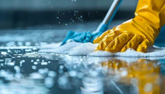 A person in yellow gloves and blue gloves cleaning a floor