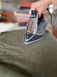 A person ironing a green shirt with a black iron