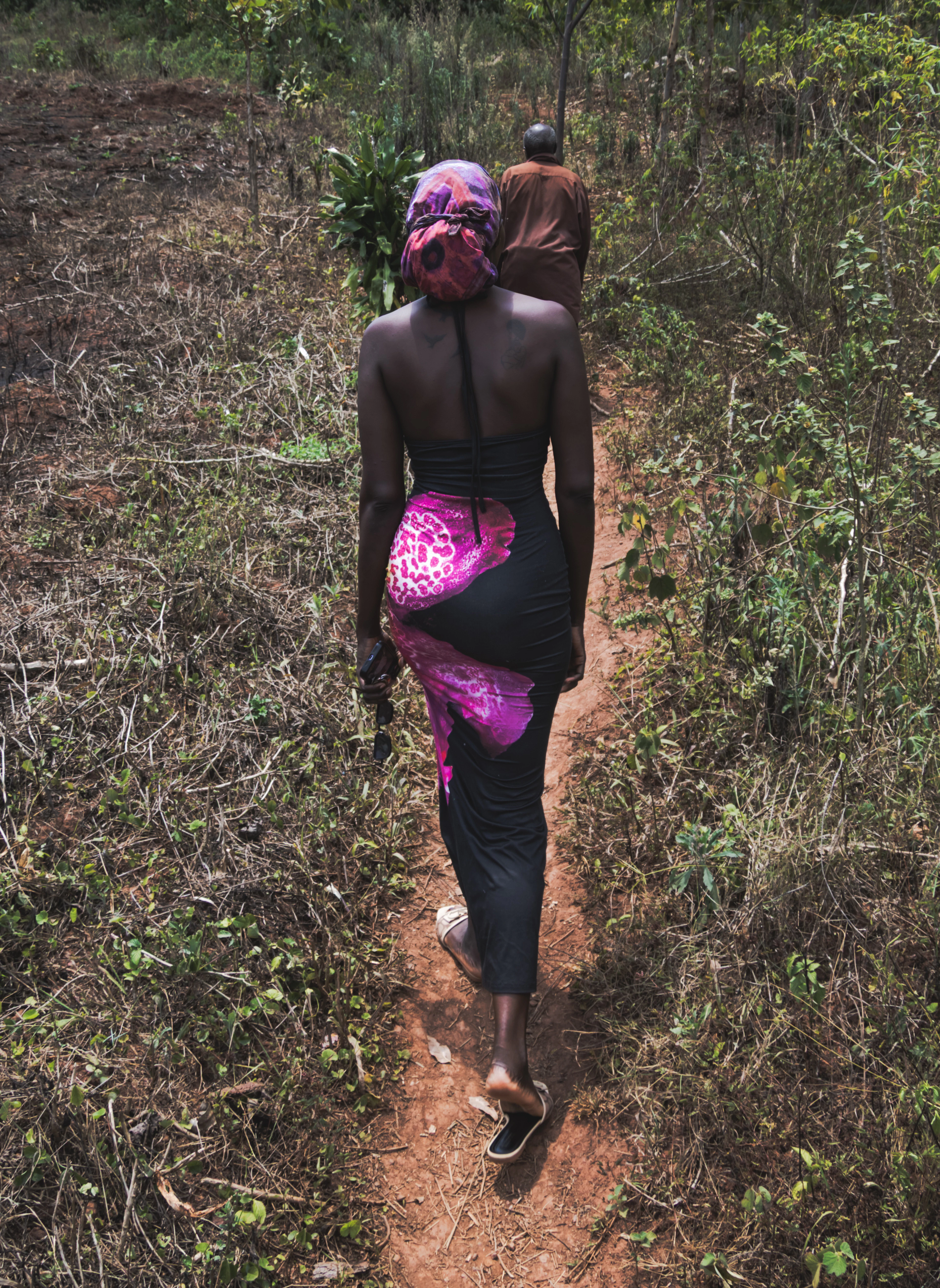 A woman walking a dirt path between green hills, seen from behind