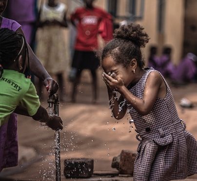 A little girl is playing with water from a faucet