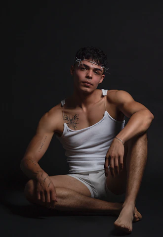 A man sitting on the ground in a white tank top