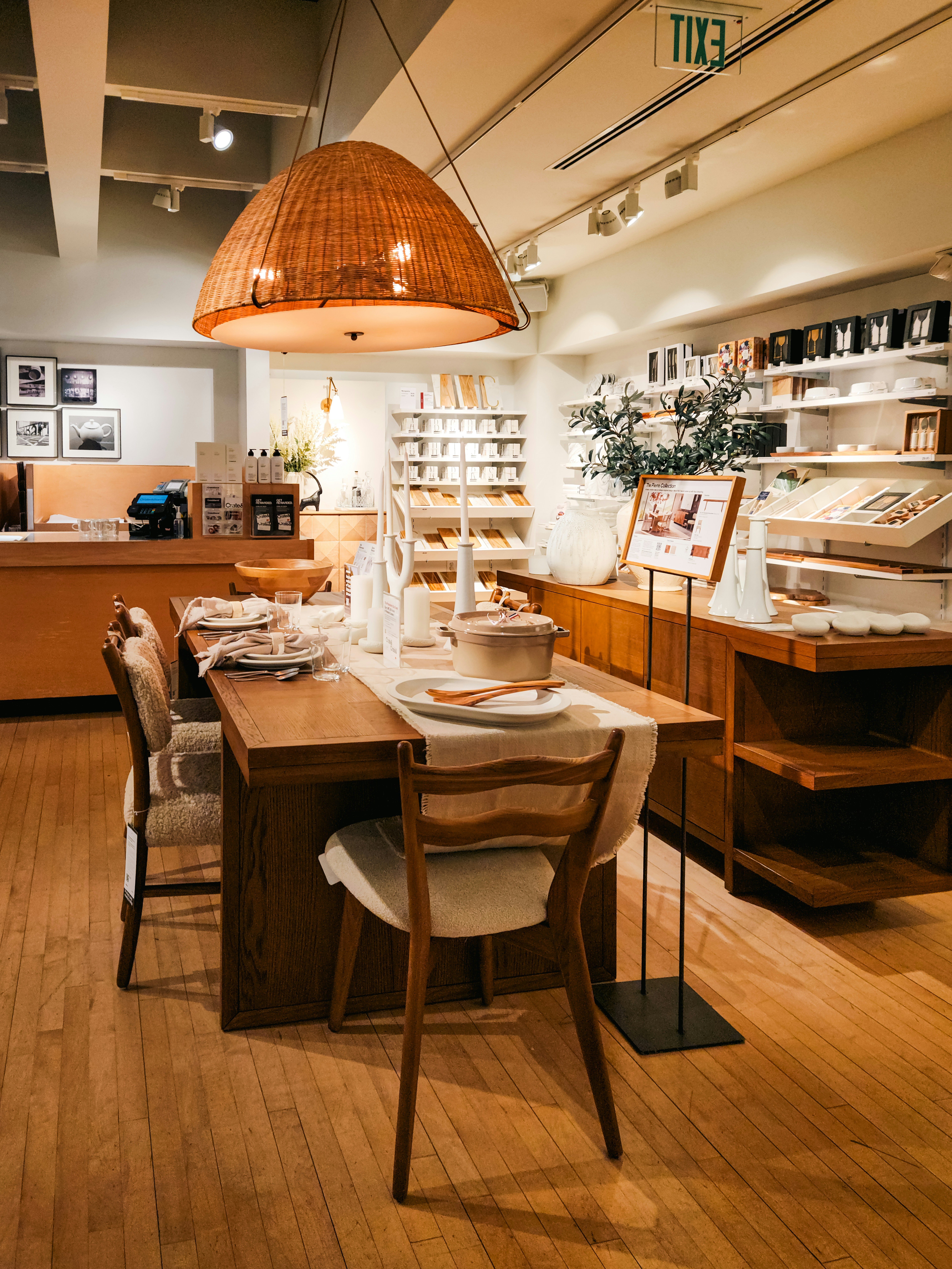 A beautifully arranged wooden dining table sits ready for a meal, set with crockery and cutlery in a neat, elegant layout. Wooden cushioned chairs encircle the table, under a stylish overhead lamp. The warm lighting creates a cozy, inviting atmosphere, making the space feel both intimate and sophisticated.