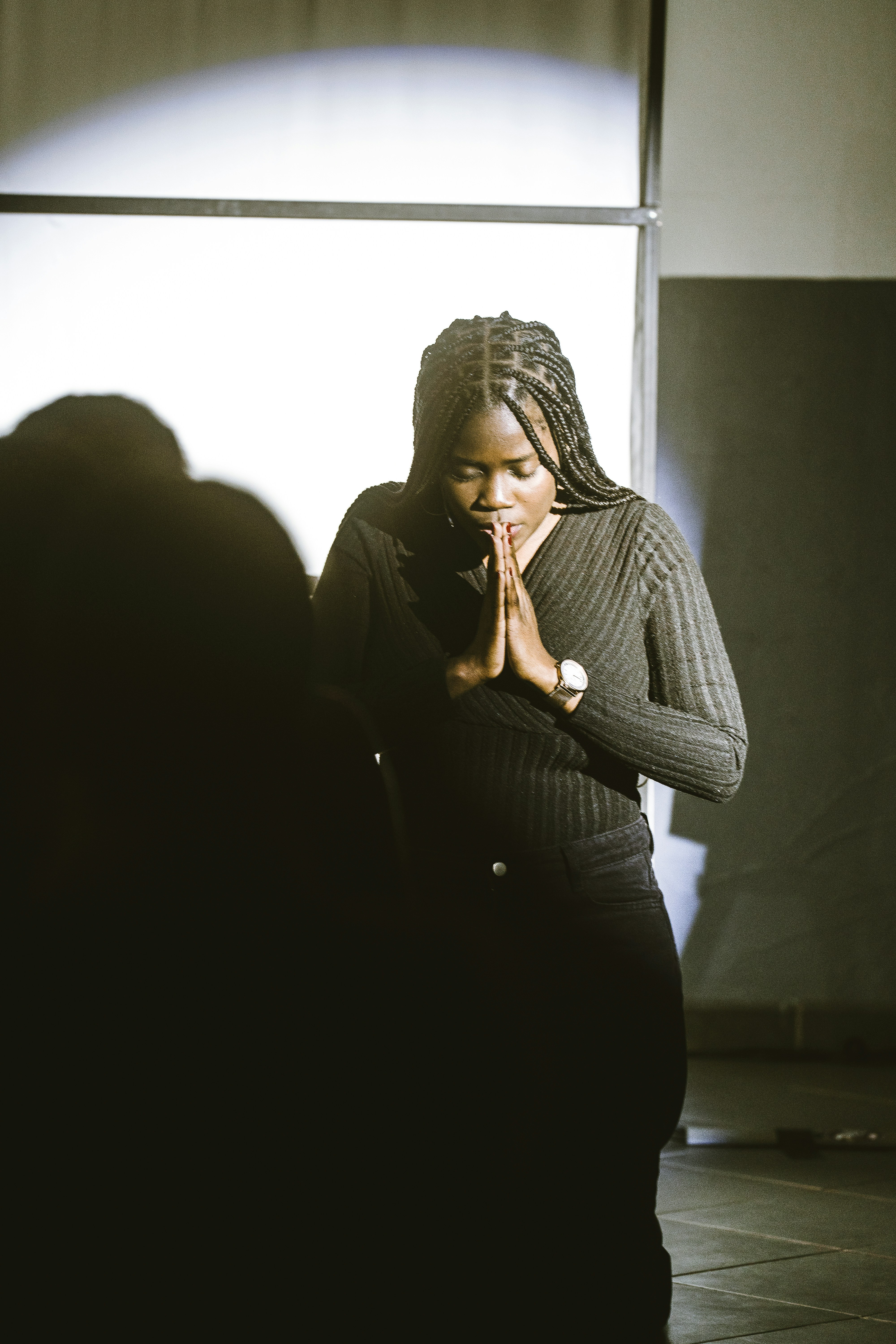 A woman standing in a dark room with her hands clasped