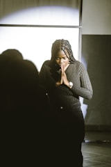A woman standing in a dark room with her hands clasped