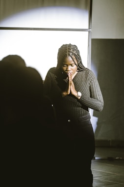 A woman standing in a dark room with her hands clasped