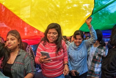 A group of people standing around a rainbow colored umbrella