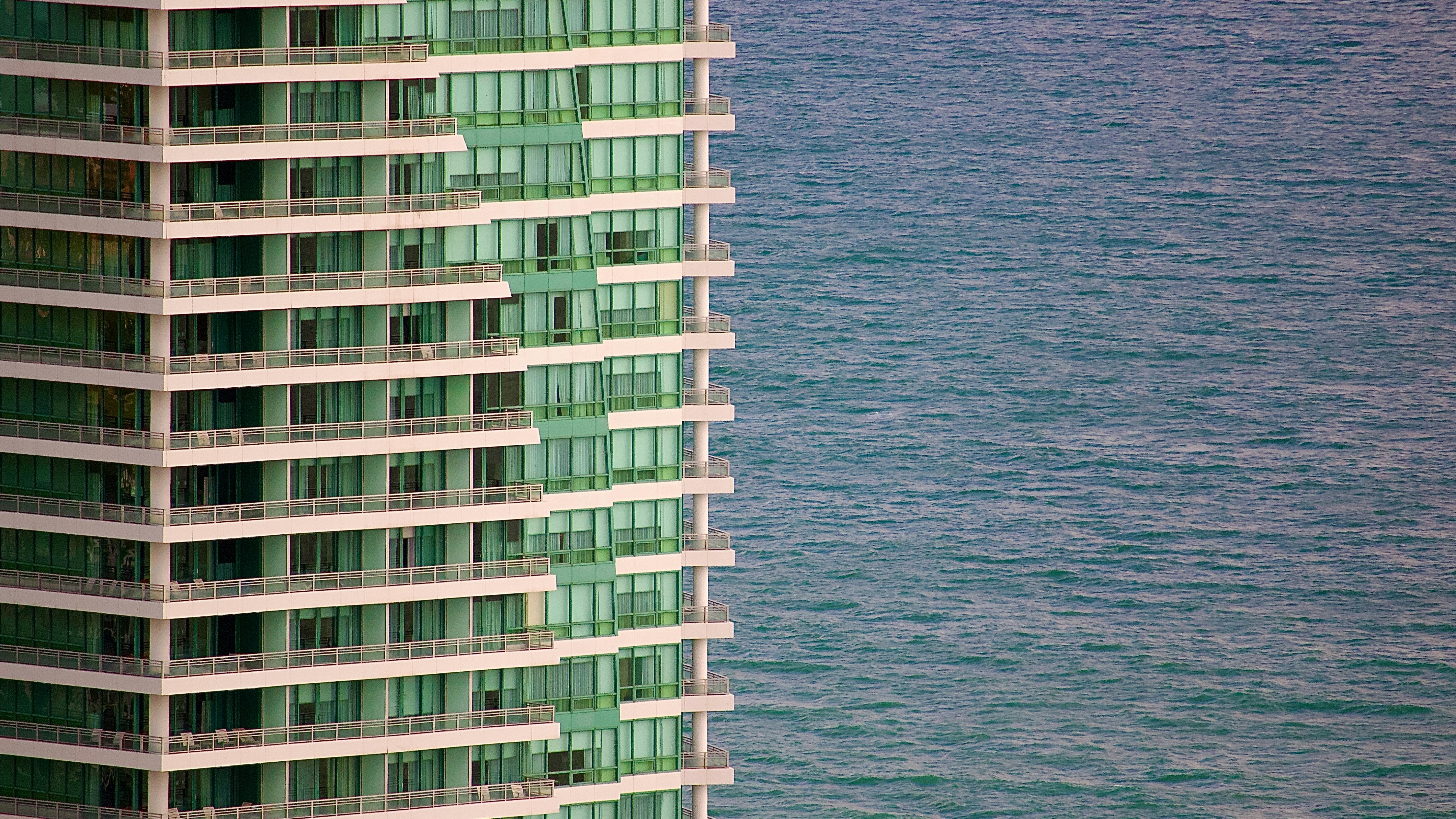 A tall building stands beside the ocean. photo – Free Urban Image on ...