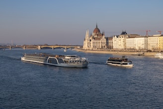 Boats sail on a river with a city backdrop.