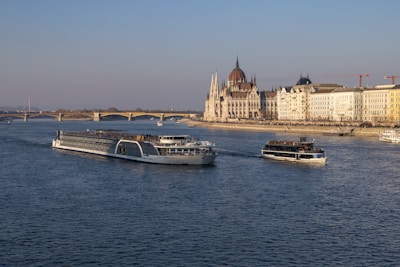 Boats sail on a river with a city backdrop.