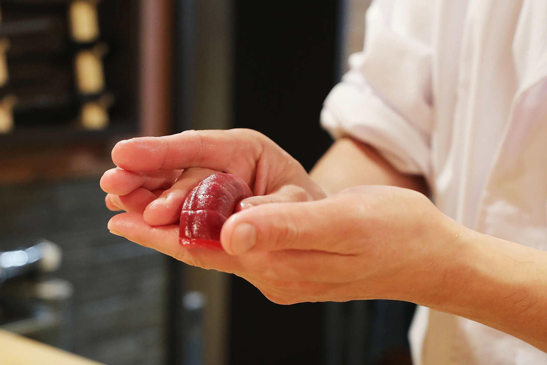 Sushi chef holding a piece of fresh sashimi during raw fish preparation