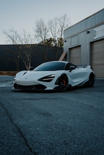 A white mclaren is parked in front of a garage.