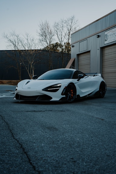 A white mclaren is parked in front of a garage.