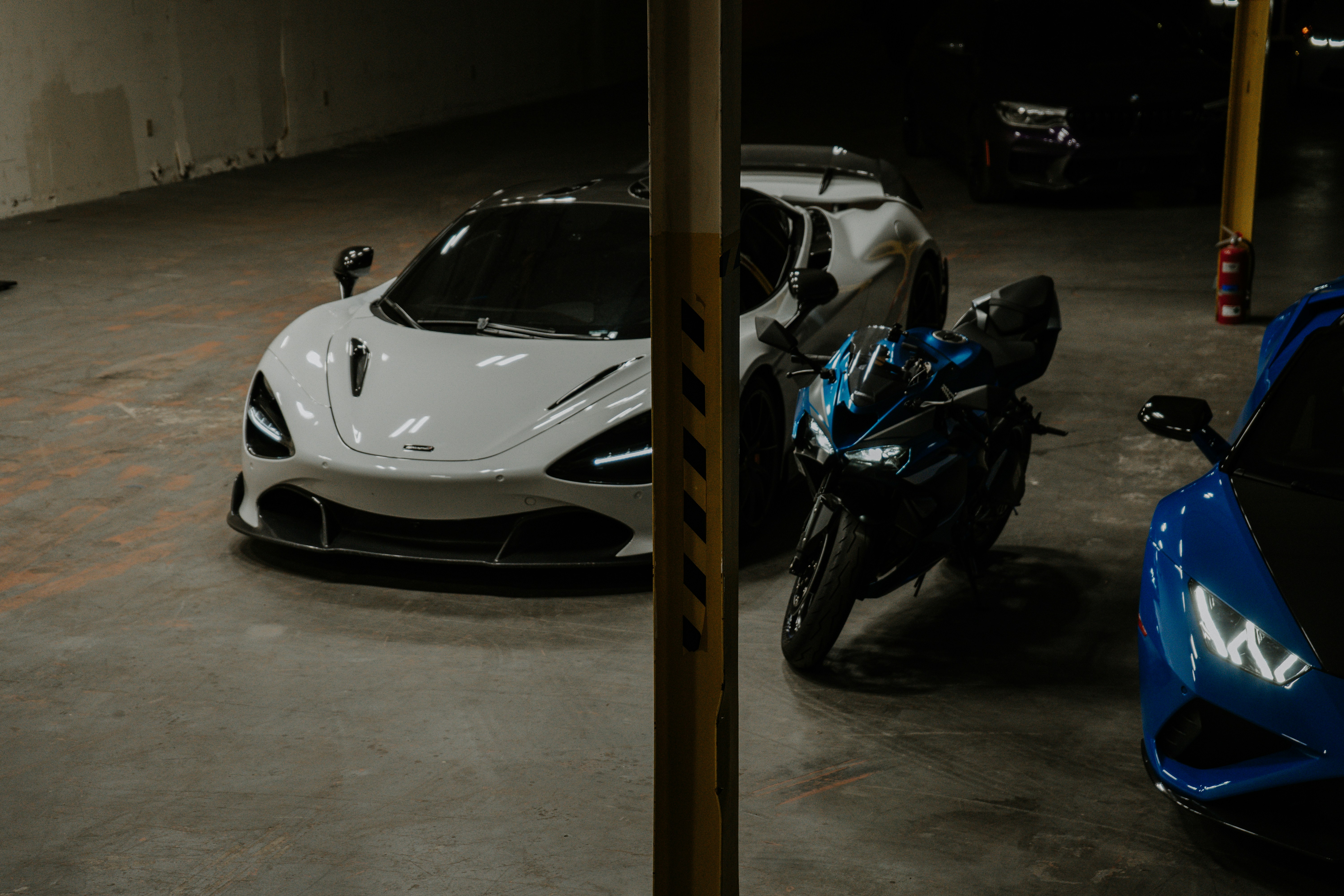 Luxury cars and a motorcycle in a dimly lit garage.