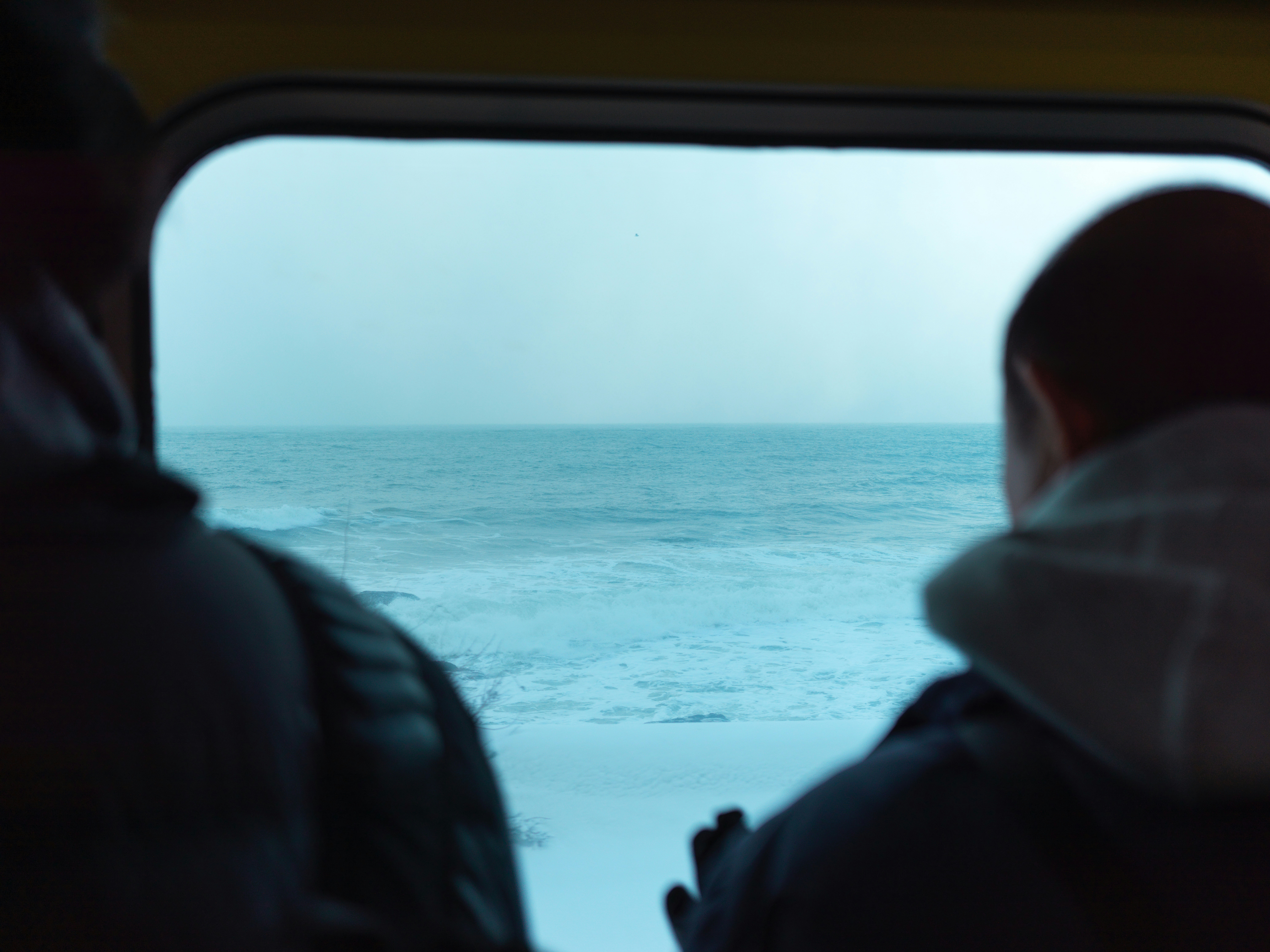 窓の外に嵐の海を眺める人々。