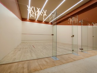 Here's a caption: an empty squash court with glass walls.