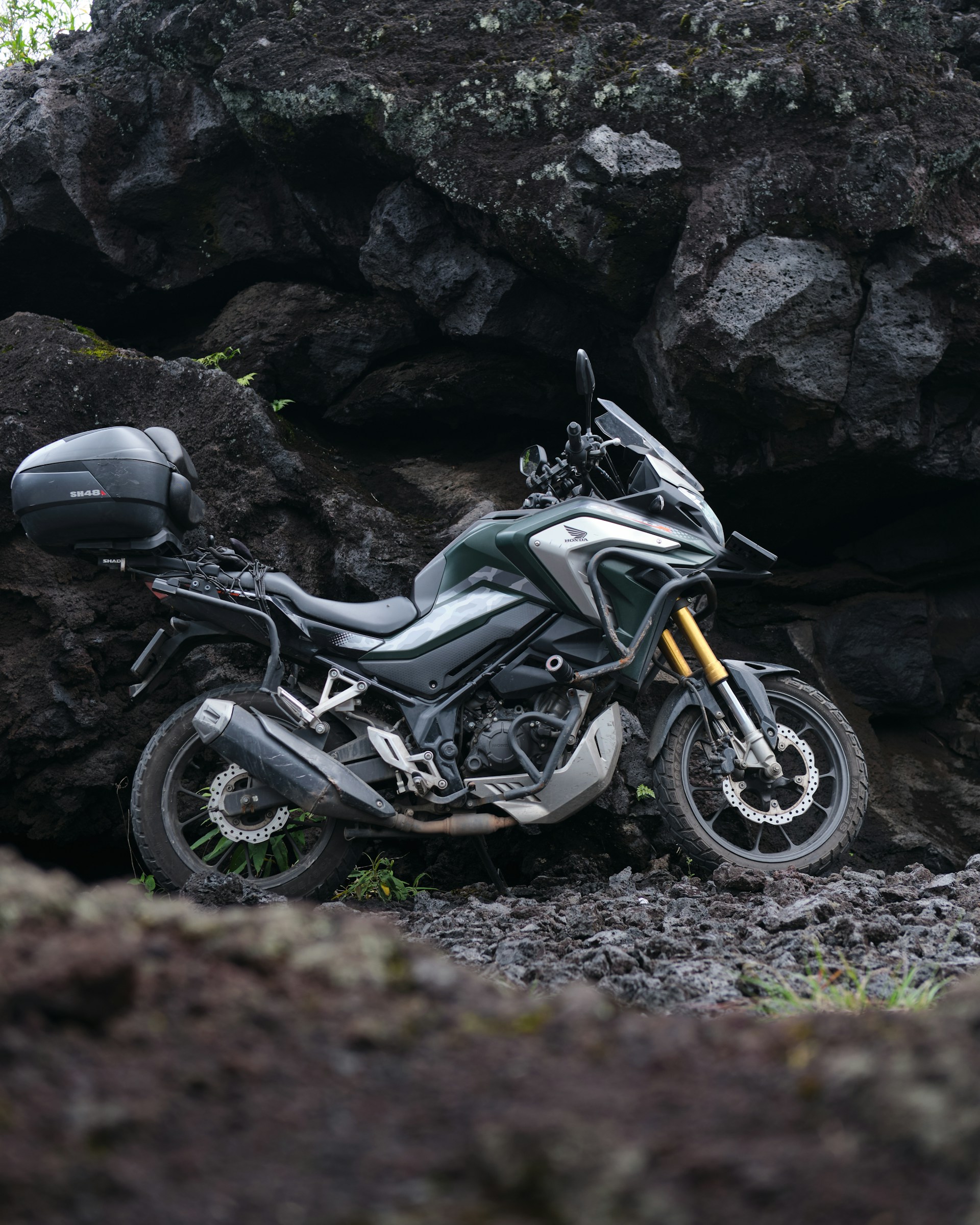 A motorcycle parks by volcanic rocks.