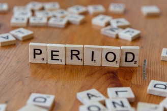 A wooden table topped with scrabble tiles spelling period