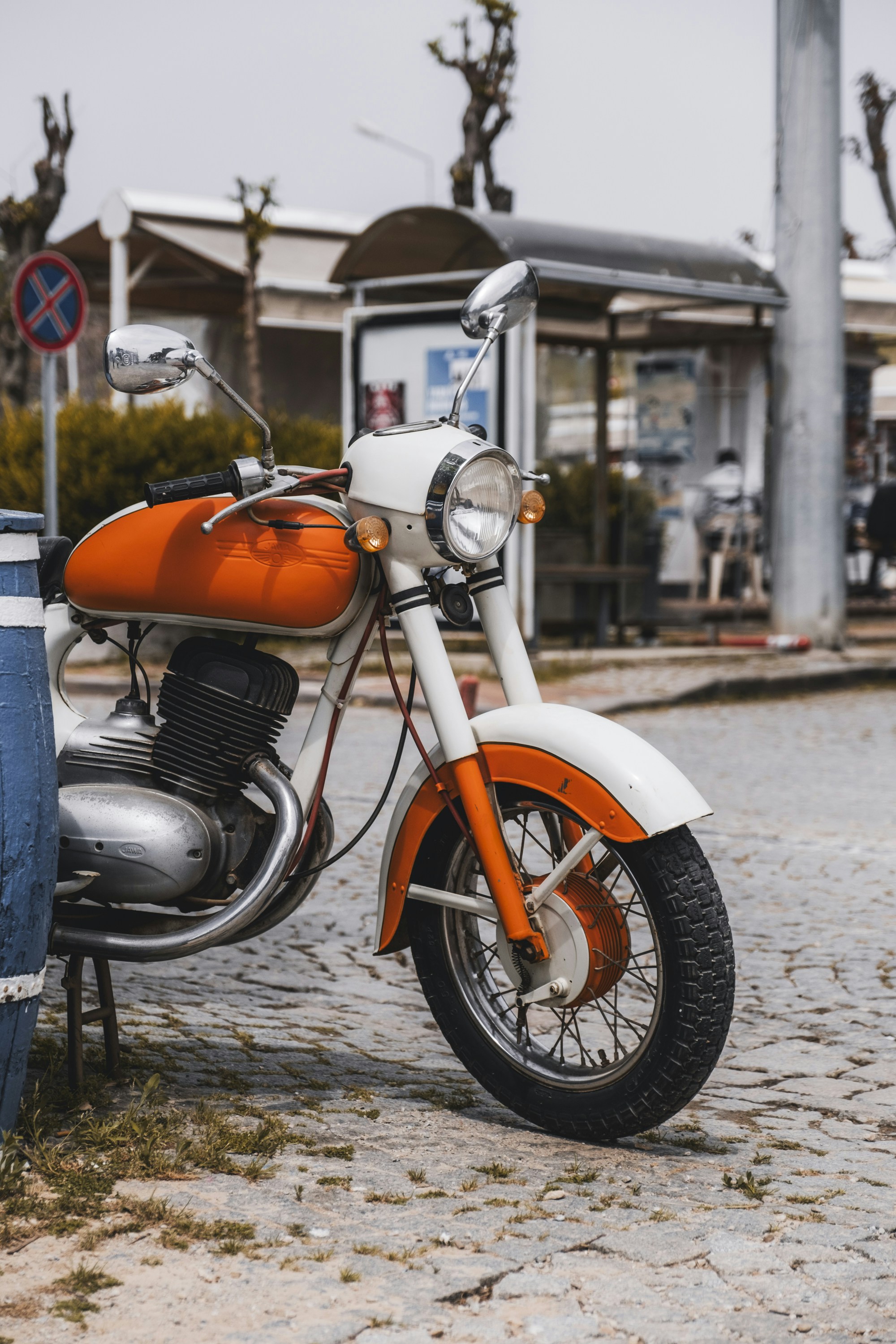 A retro orange and white motorcycle parked outdoors.