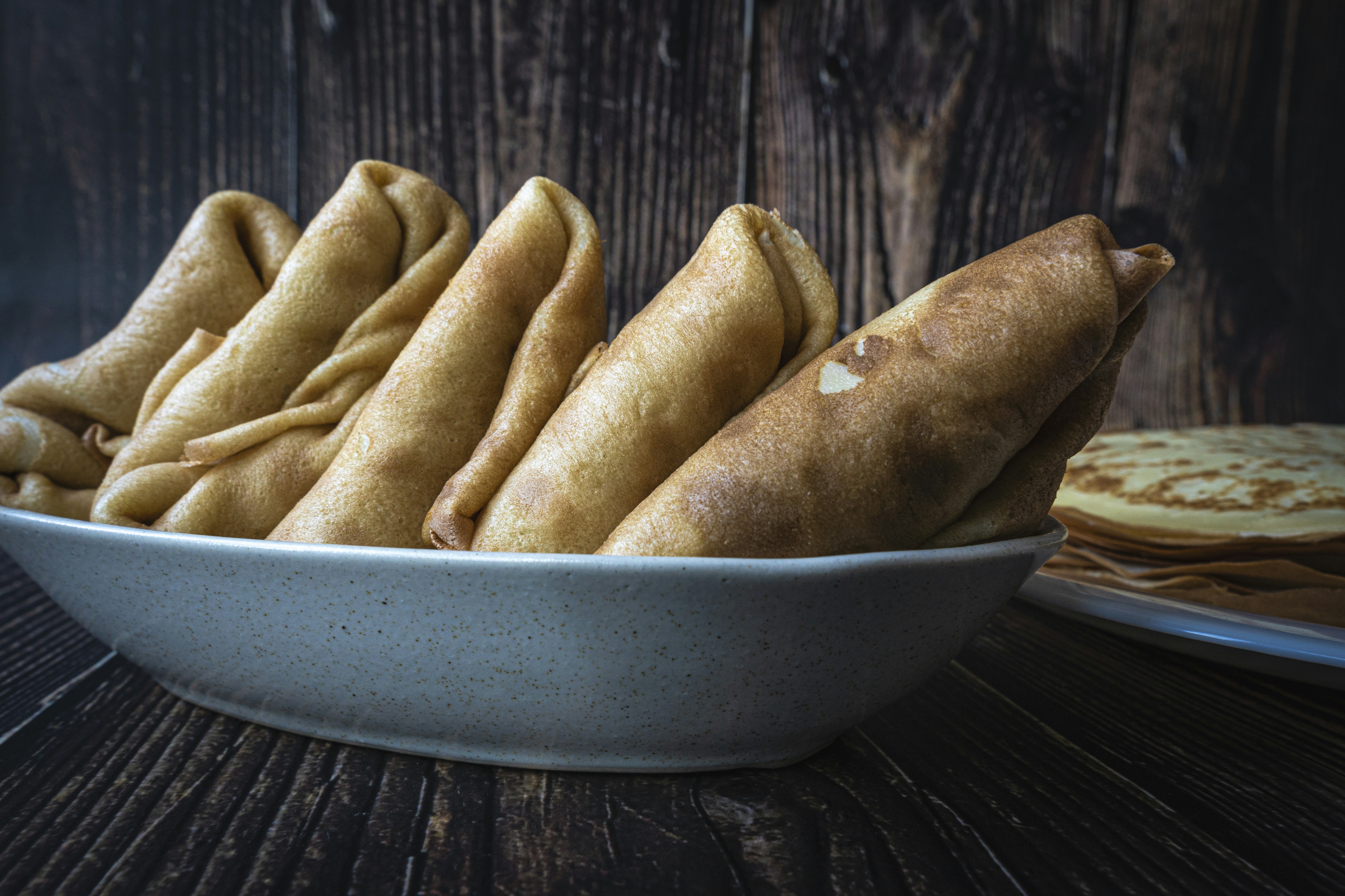 A white bowl filled with food next to a plate of pancakes