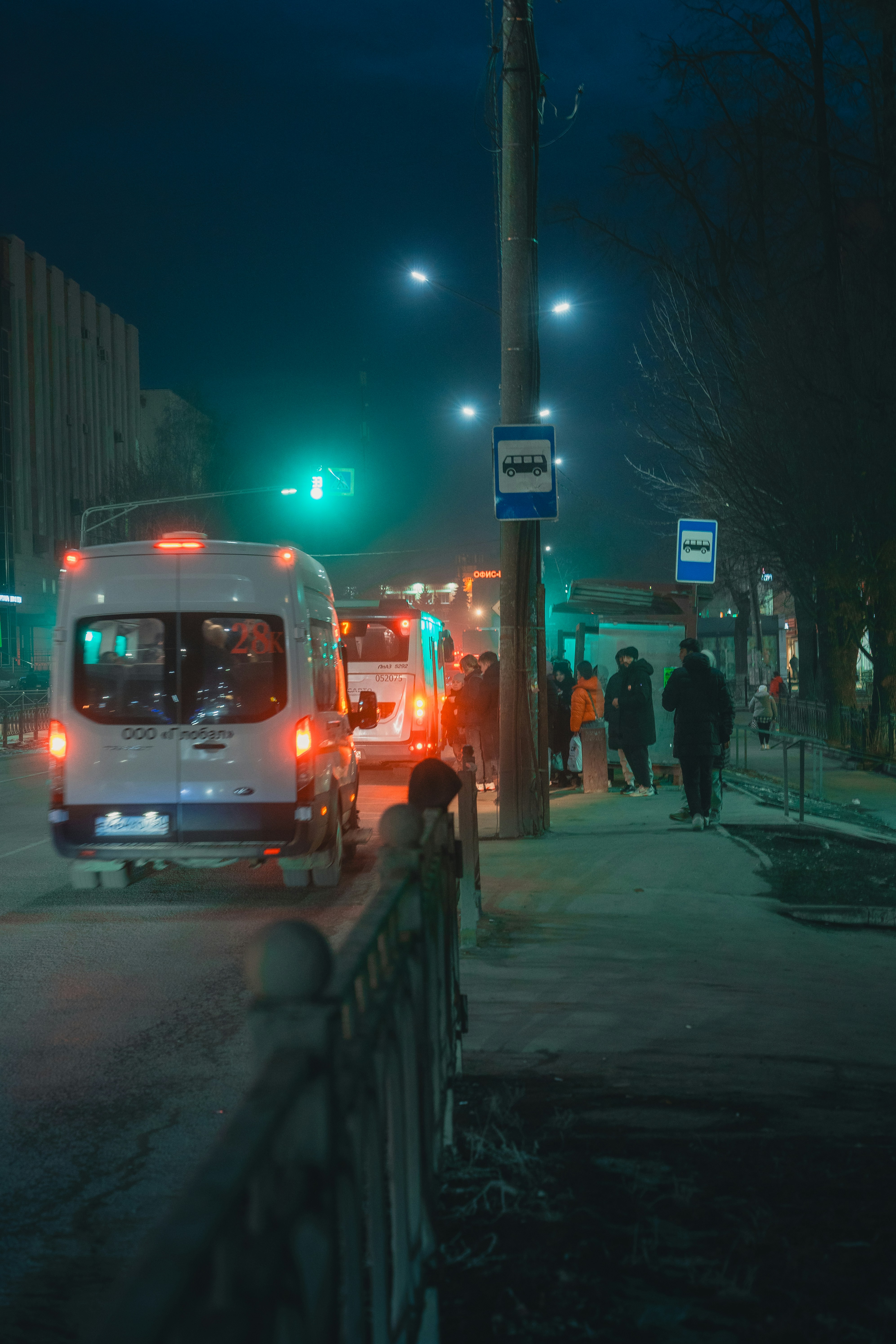 A bus stop at night with people waiting.