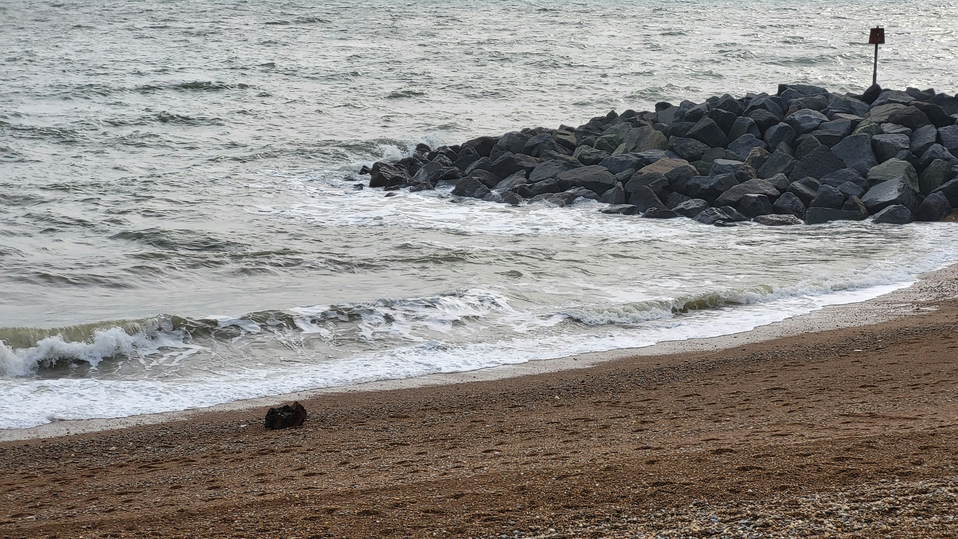 Waves crash onto a sandy beach with rocks.